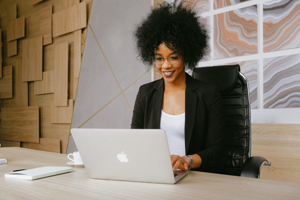 woman in black blazer sitting by the table while using macbook